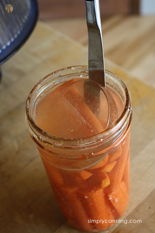 Using a knife to remove the glass weight from a jar of fermented carrots.