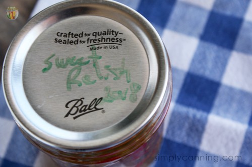 A sealed jar of pickle relish with its contents and date labeled on the lid.