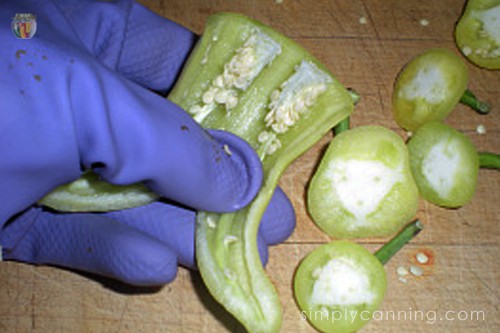Removing seeds from a halved pepper using a gloved hand.