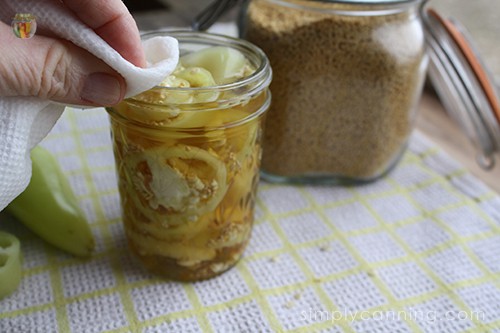 Wiping the rim of a jar filled with pepper rings and brine.