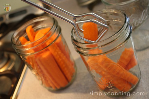 Putting crinkle cut carrots into canning jars using a pair of tongs.