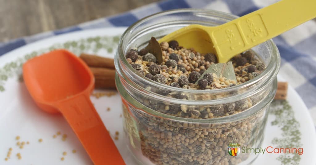 A jar of mixed pickling spice with a measuring spoon in it.