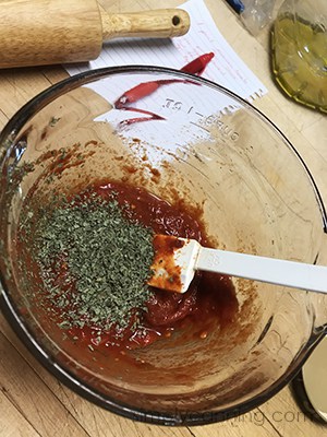 Using a white spatula to stir the dried herbs into the tomato sauce.