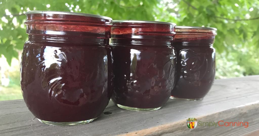Three jars of plum jam on a deck railing.