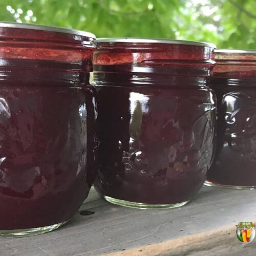 Three jars of plum jam on a deck railing.