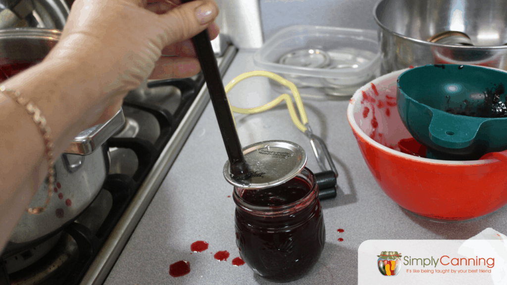 Placing the flat canning lid on the jar using a magnetic lid lifter.