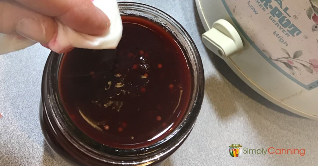 Wiping the rim of a filled jar of plum sauce with a wet paper towel.