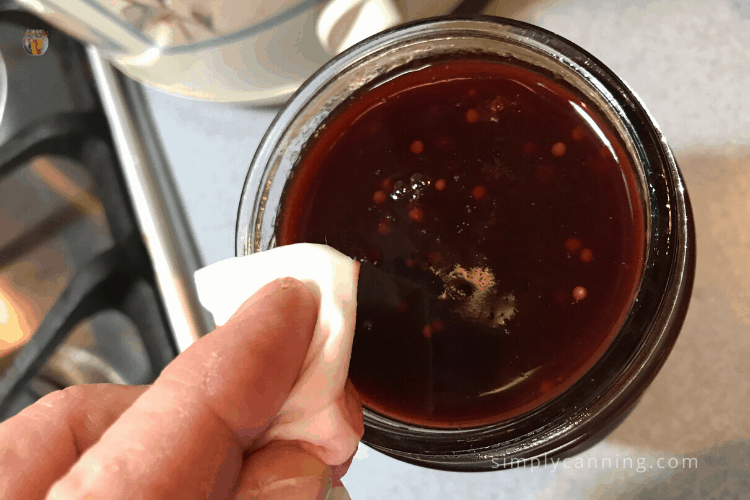 Wiping the rim of a jar of plum sauce with a wet paper towel.