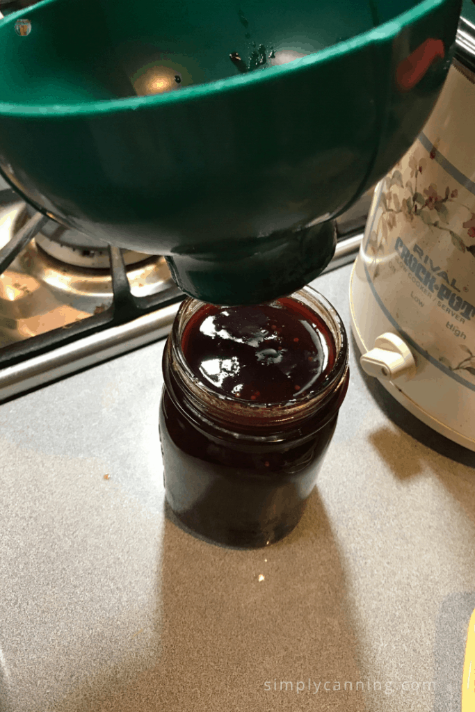 Lifting the canning funnel off a full jar of plum sauce.