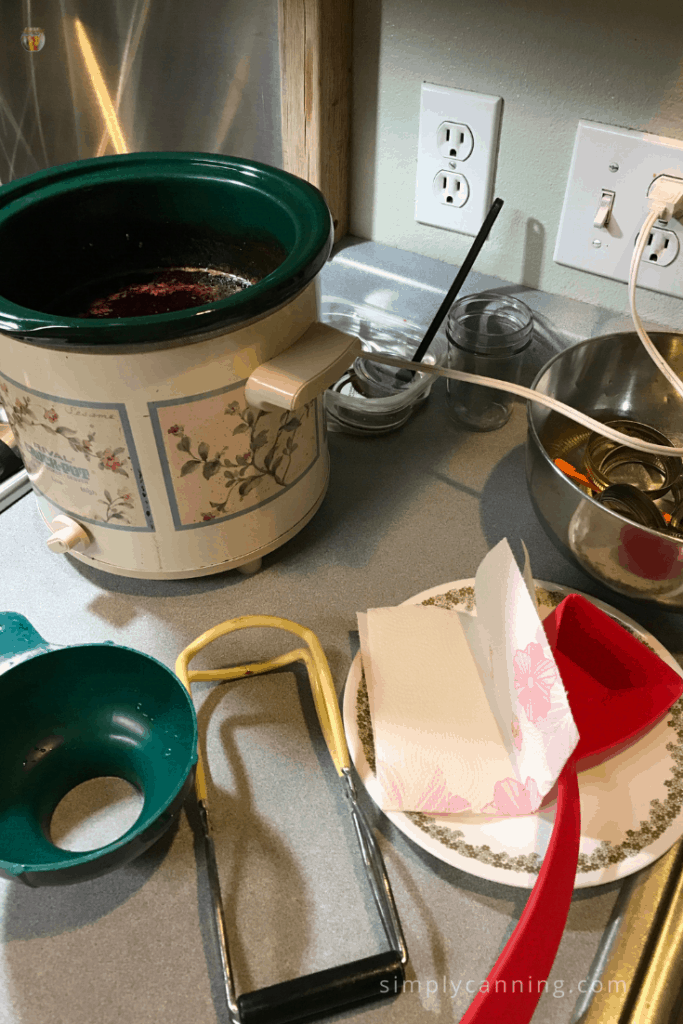 Cooking down the plum sauce in the CrockPot with various canning supplies on the counter around the crock.