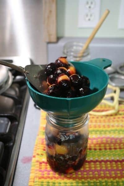 Spooning cooked plums into a pint sized canning jar through a canning funnel.