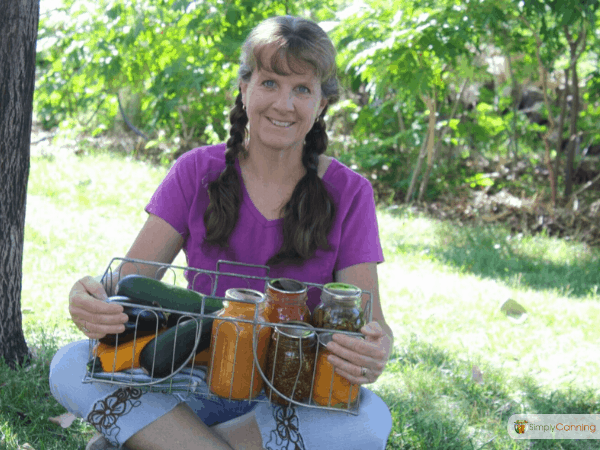 Sharon in braids holding a basket of home canned food while sitting outdoors under a tree.