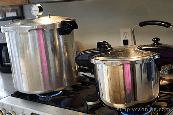 Presto pressure canner sitting on the stove next to a pressure cooker that is smaller than the canner.