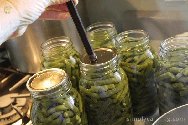 Placing flat jar lids on the jars of green beans.