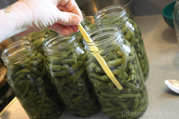 Removing air bubbles from jars of green beans.