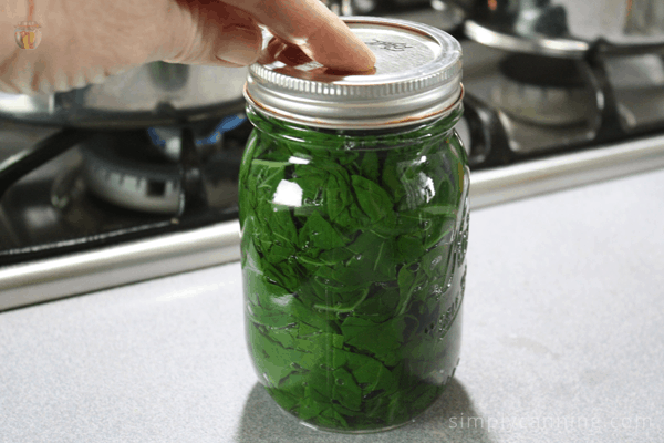 Tightening the lid on a jar of canned greens.