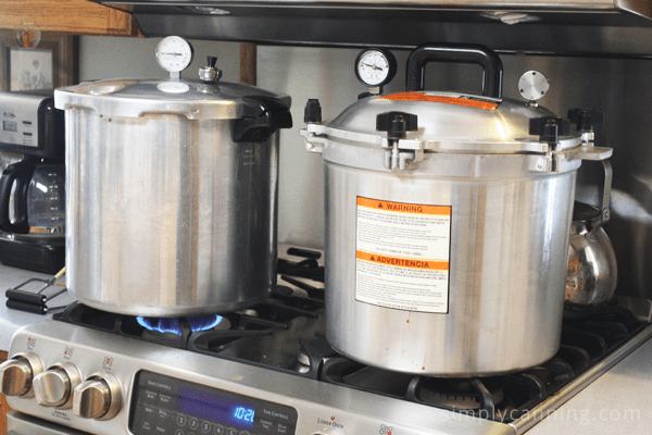 Presto and All American pressure canners sitting on a stovetop.