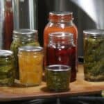 Jars filled with home canned food sitting next to a shiny canner.