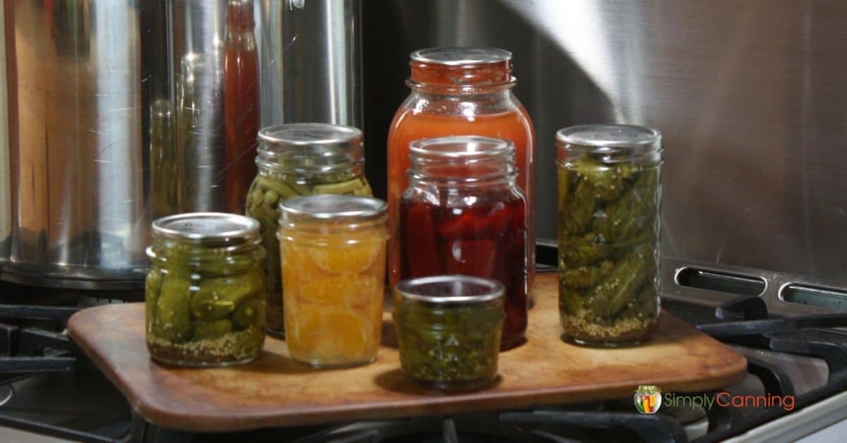 Jars filled with home canned food sitting next to a shiny canner.