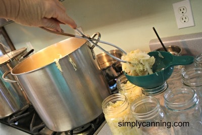 Filling jars with sauerkraut using tongs and a green canning funnel.
