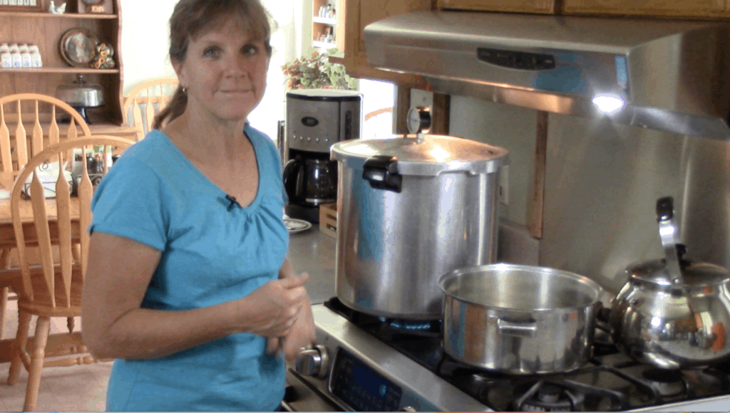 Sharon wearing a blue shirt and standing next to a pressure canner on the stove.