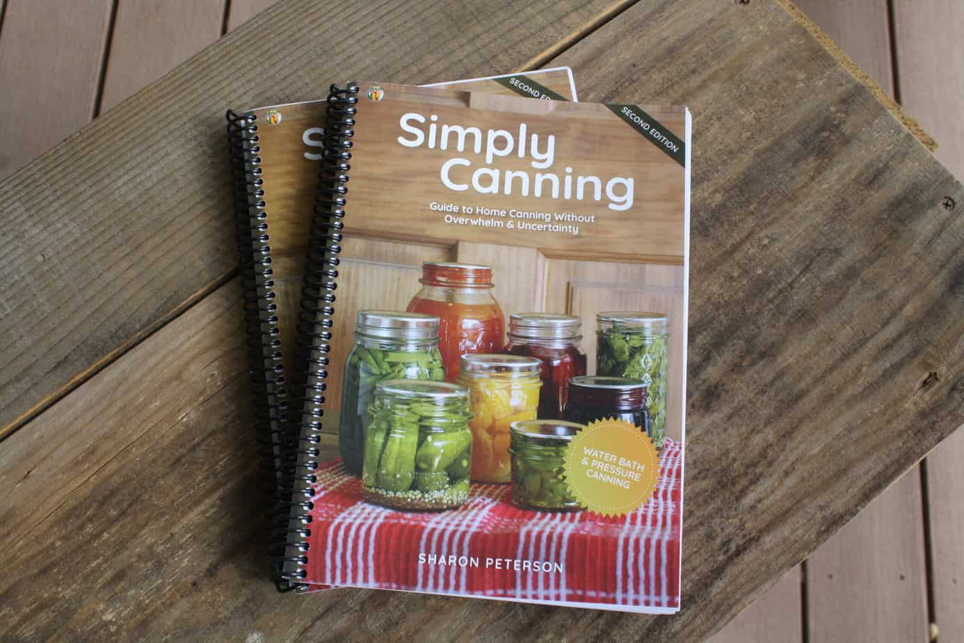 Spiral bound Simply Canning cookbooks on a wooden background.