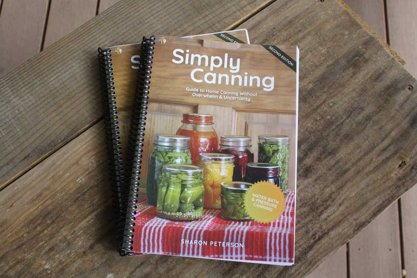 Spiral bound Simply Canning cookbooks on a wooden background.