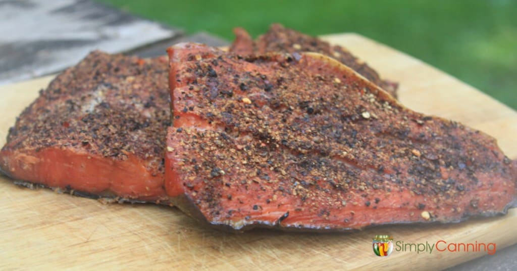 Smoked salmon coated with pepper and sitting on a wooden board.