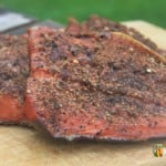 Smoked salmon coated with pepper and sitting on a wooden board.