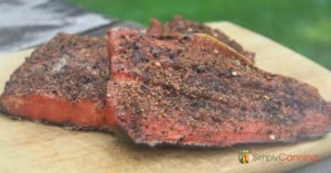 Smoked salmon coated with pepper and sitting on a wooden board.