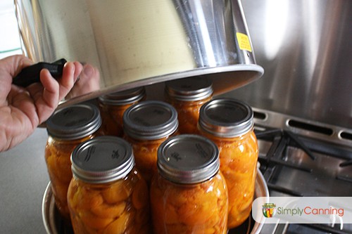 Lifting the lid of a steam canner with jars of peaches in the pot.