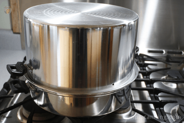 Shiny steam canner covered and sitting on the stove.