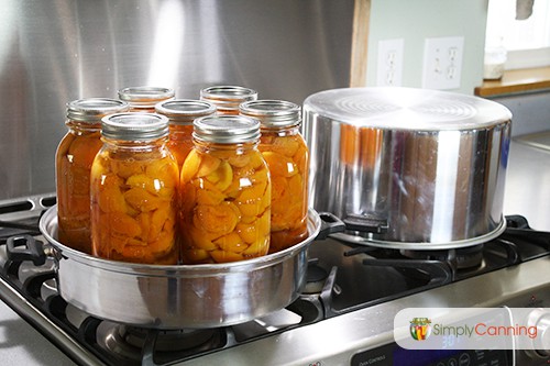Bright jars of peaches in the steam canner with the canner lid off to the side.