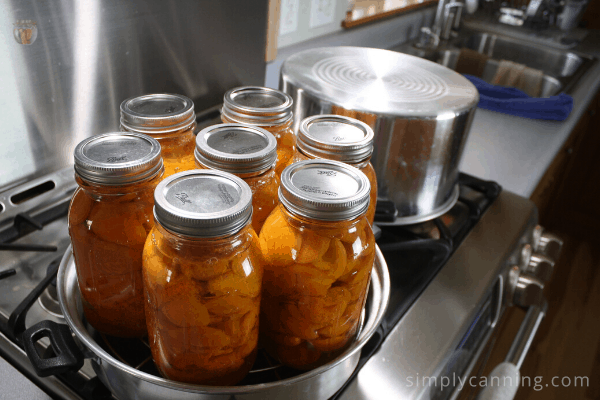 Jars filled with peaches sitting in the bottom of the steam canner.