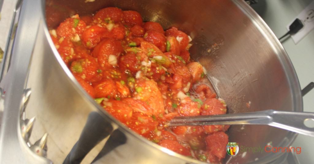 Stirring a stockpot filled with peeled tomatoes and chopped veggies.