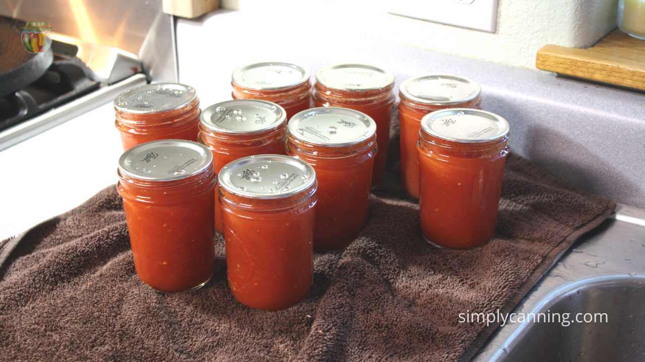 9 jars of freshly washed jars of tomato sauce on a brown towel, sitting by the sink.  