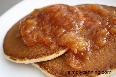 Stonefruit jam spread over golden brown pancakes on a white plate.