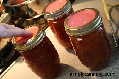 Placing reusable lids on top of the jars of stonefruit jam.