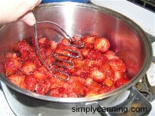 Mashing strawberries with a potato masher.