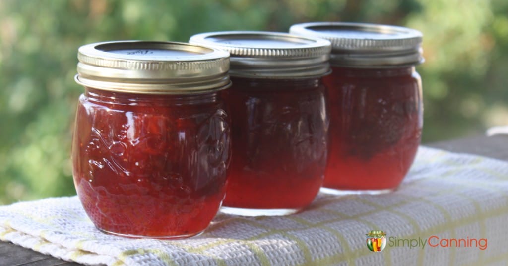 Three small jars of red strawberry jam.