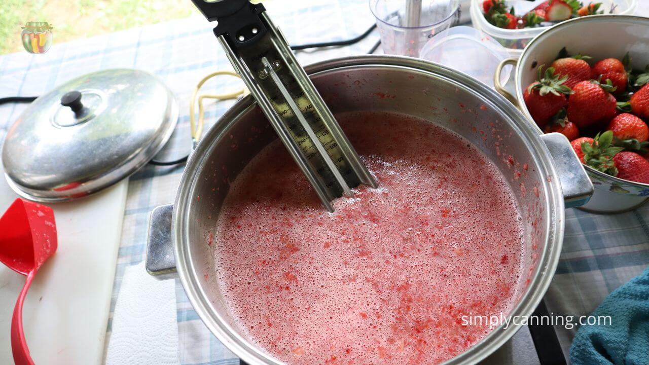Pot of strawberry lemonade concentrate heating up with a candy thermometer monitoring temperature. 