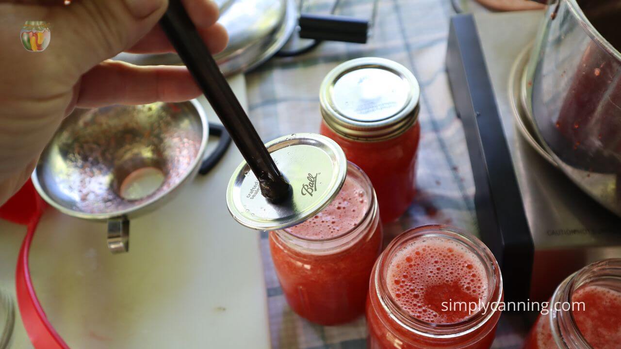 3 pint jars strawberry lemonade concentrate on the table, a canning lid being placed on one jar.  