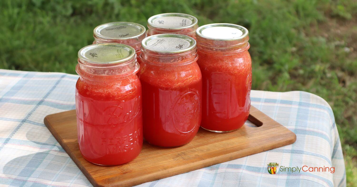 5 jars of homemade strawberry lemonade concentrate sitting on a small cutting board on the picnic table.  