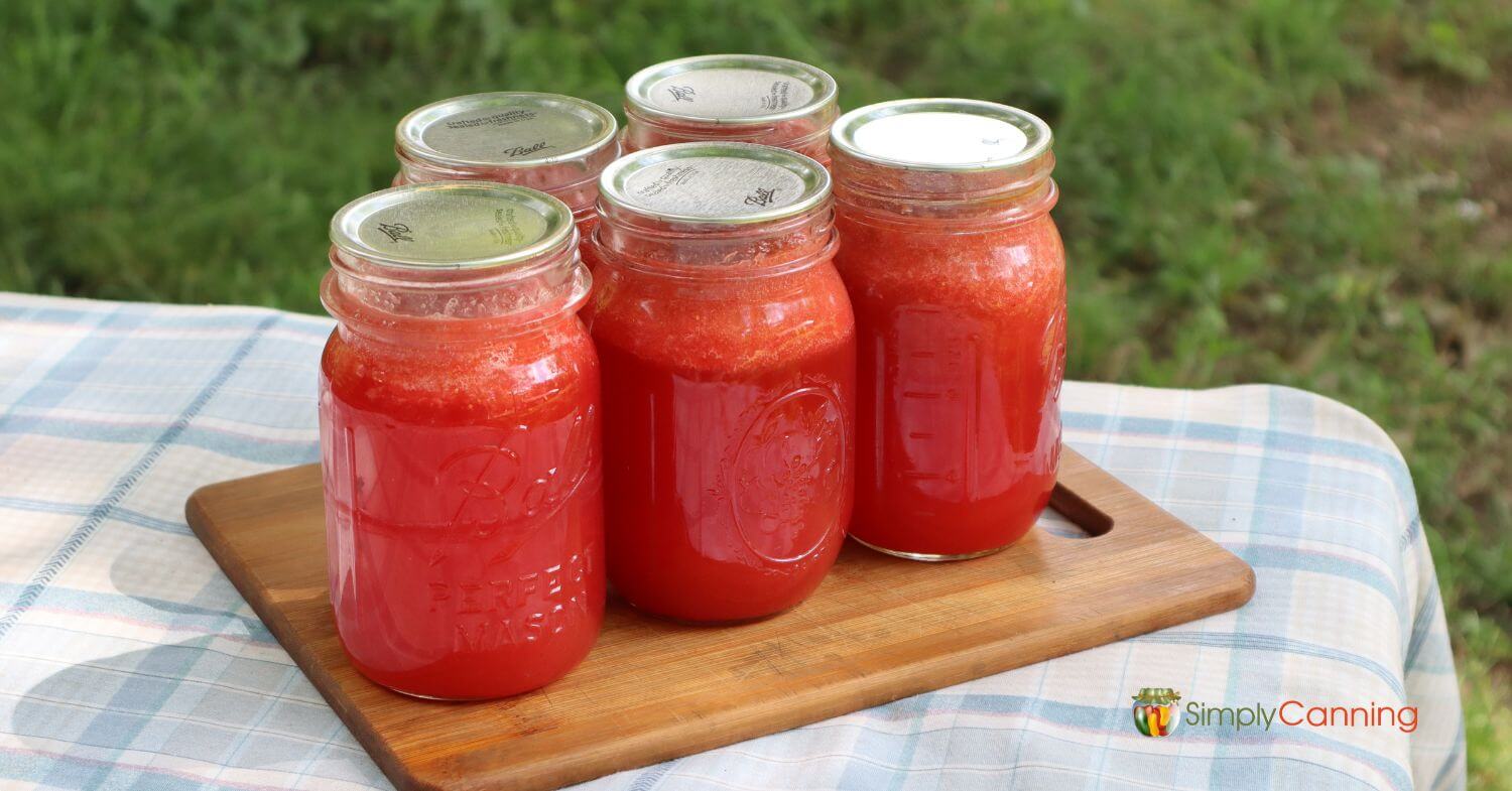 5 jars of homemade strawberry lemonade concentrate sitting on a small cutting board on the picnic table.