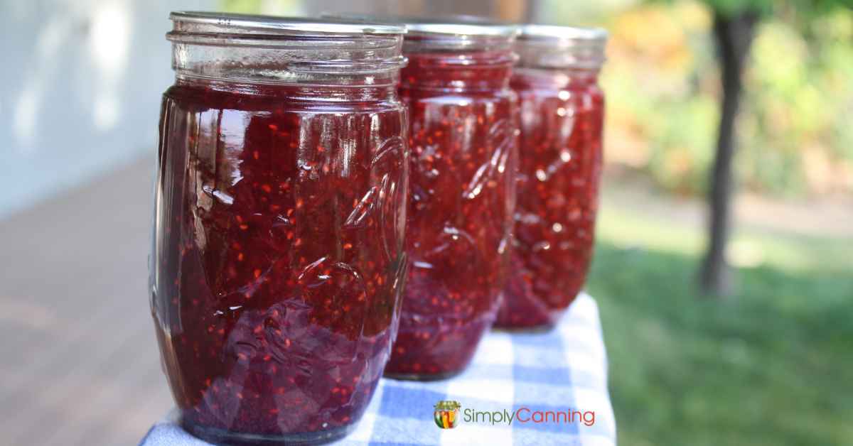 3 jars of homemade mixed berry jam sitting on the railing of a deck.