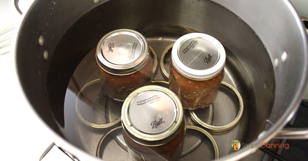 Jars sitting in a canner of water with rings making a homemade rack at the bottom.