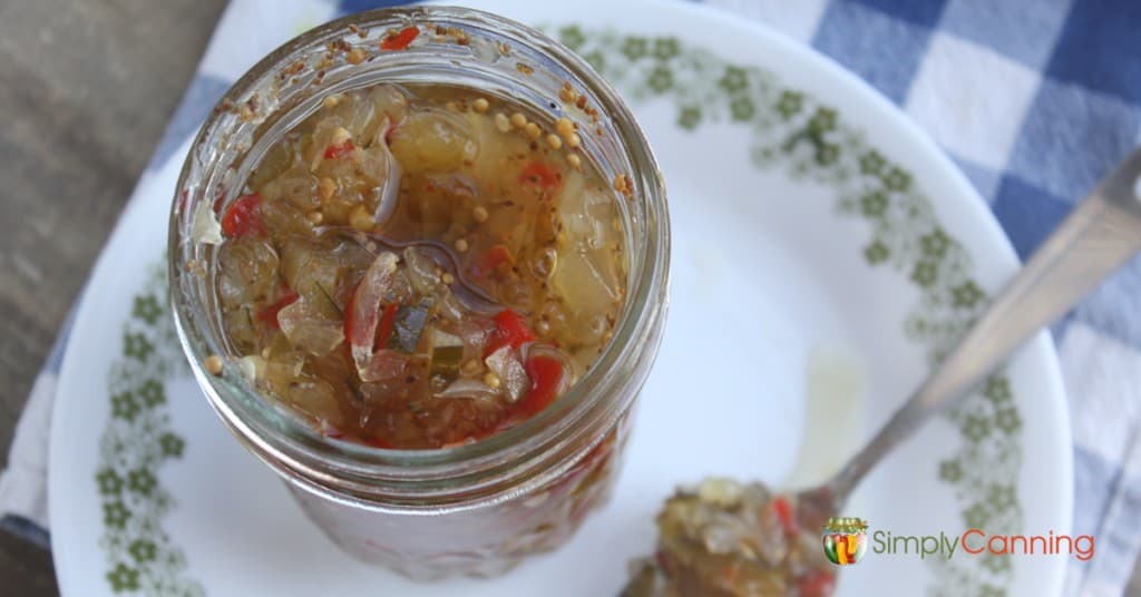 An open jar of green and red pickle relish with a spoonful of relish on the side.