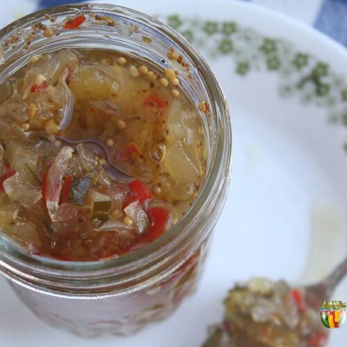 An open jar of green and red pickle relish with a spoonful of relish on the side.