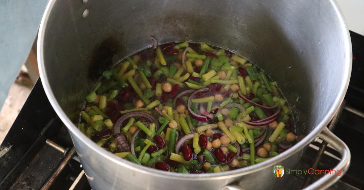 Top down view of a small white square serving dish with three bean salad, green beans, pinto beans, garbanzo beans, some onions, all on a blue plate with a fork to the side.