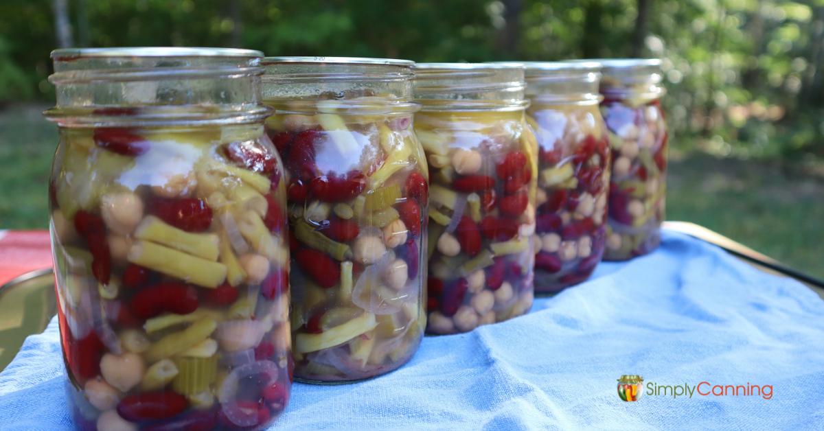 5 pint jars of home canned 3 bean salad lined up on a blue table cloth.